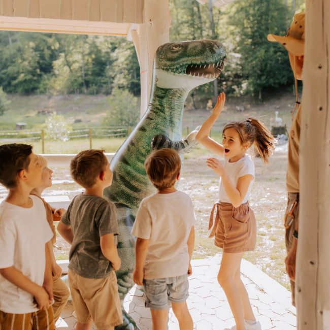 Kinder spielen mit einem aufblasbaren Dinosaurier während eines Dinogeburtstags.