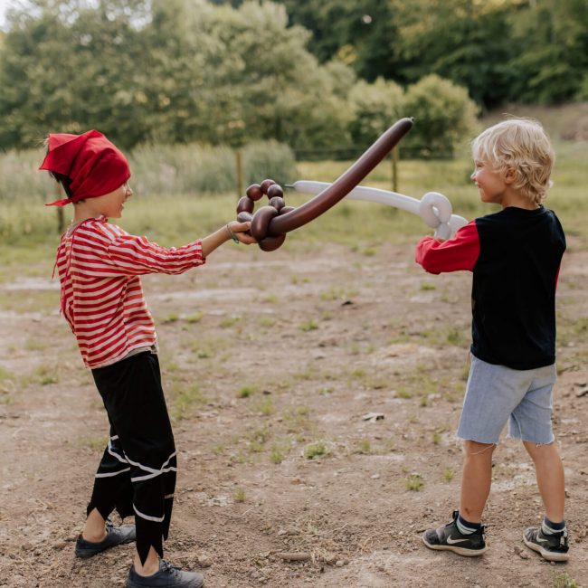 Zwei als Piraten verkleidete Kinder kämpfen mit Luftballonschwertern.