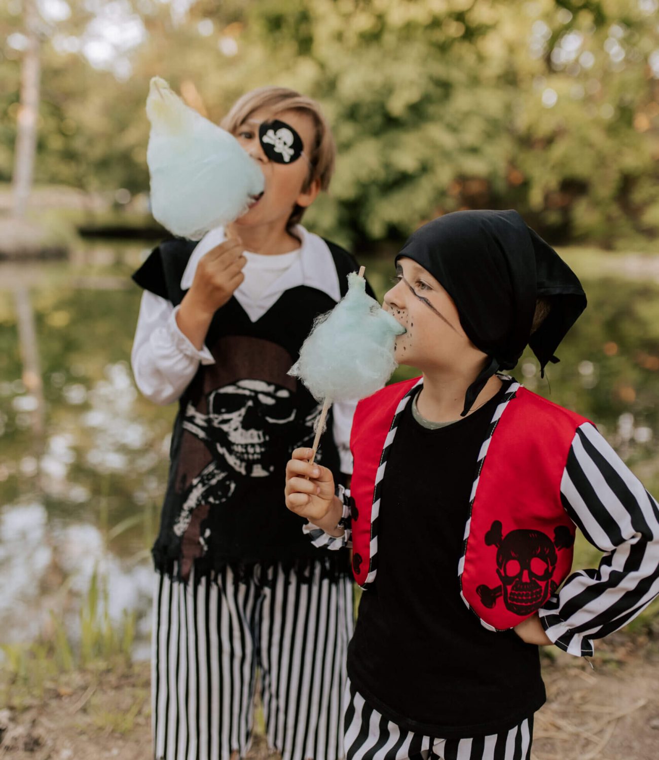 Zwei als Piraten verkleidete Kinder essen Zuckerwatte vor dem See der Villa Sophie.